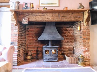 A brick fireplace with a black wood stove and wooden mantel with decorative items at The Bridewell in Woodbridge
