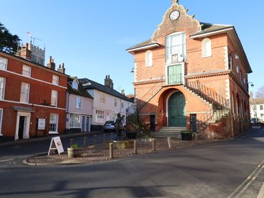 A historic brick building with an external staircase and a clock above a green door at The Bridewell in Woodbridge