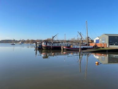 A harbor with boats docked near buildings and trees across the water at The Bridewell in Woodbridge