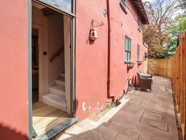 An outdoor patio area with a red exterior wall two windows and two chairs with a small table at The Bridewell in Woodbridge