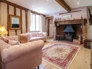 A living room with pink sofas a patterned rug and a fireplace with wooden beams at The Bridewell in Woodbridge