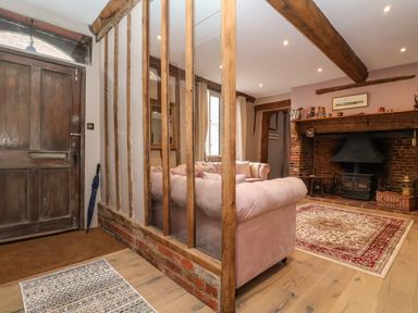 An entryway with a wooden door next to a living room with pink sofas and a fireplace at The Bridewell in Woodbridge