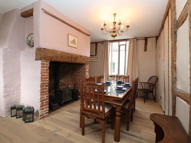 A dining room with a wooden table and chairs next to a fireplace and a window at The Bridewell in Woodbridge
