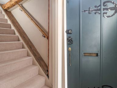 A carpeted staircase with wooden handrail next to a blue door with metal decorations at The Bridewell in Woodbridge