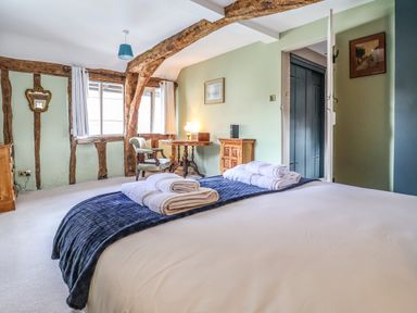 A bedroom with a bed folded towels wooden furniture and exposed wooden beams at The Bridewell in Woodbridge