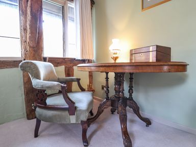 A wooden table with a lamp and wooden box next to an upholstered armchair near a window at The Bridewell in Woodbridge