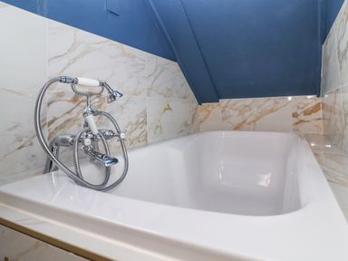 A bathtub with a handheld showerhead and hot and cold faucets under a slanted blue ceiling at The Bridewell in Woodbridge