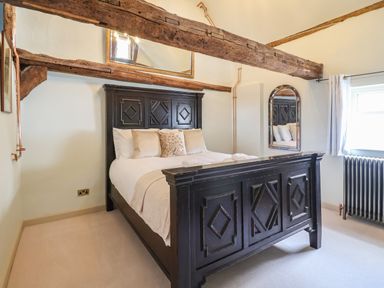 A bedroom with a dark wooden bed frame pillows mirror window and wooden ceiling beams at The Bridewell in Woodbridge