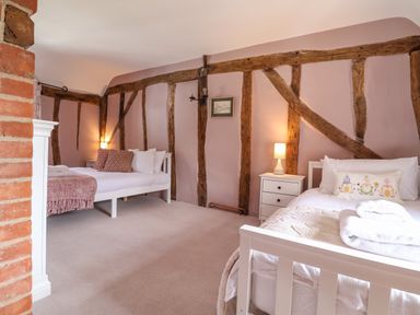 A bedroom with two white beds bedside tables lamps and exposed wooden beams on walls at The Bridewell in Woodbridge
