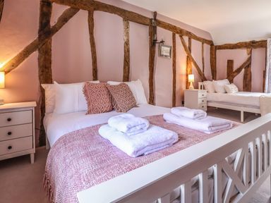 A bedroom with two beds side by side with wooden beams on the walls and bedside tables with lamps at The Bridewell in Woodbridge