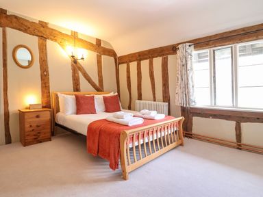 A bedroom with a wooden bed frame two red pillows and a red blanket next to a nightstand with a lamp at The Bridewell in Woodbridge