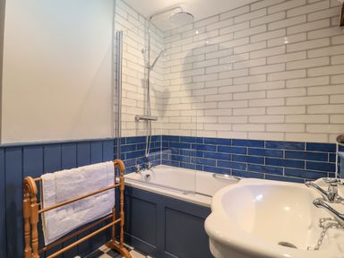 A bathroom with a bathtub shower with white and blue tiled walls a wooden towel rack and a white sink at The Bridewell in Woodbridge