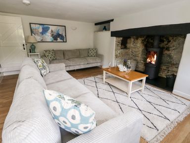 A living room with two sofas a coffee table with glasses and bottle a wood burning stove and a rug at Dairy Cottage in Abbotsbury