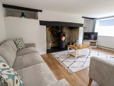 A living room with a stove fire a coffee table a TV a sofa and armchair at Dairy Cottage in Abbotsbury