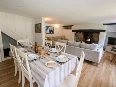 A dining table set with plates and a living area with sofas and a fireplace at Dairy Cottage in Abbotsbury