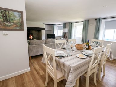 A dining table set with plates glasses a bottle and bowls in a living room with sofas fireplace and television at Dairy Cottage in Abbotsbury