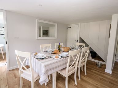 A dining room with a table set for six people and white chairs at Dairy Cottage in Abbotsbury