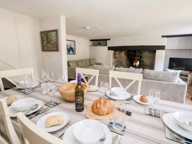 A dining table set with plates glasses bread and a bottle in a living room with sofas a fireplace and a television at Dairy Cottage in Abbotsbury