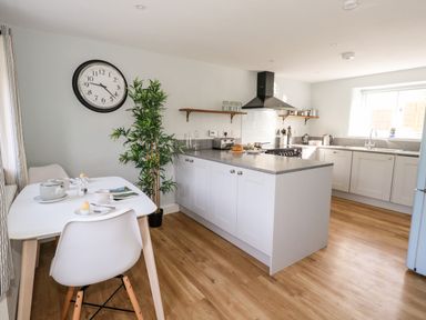 A kitchen with island, stove, sink, dining table with chairs and a wall clock at Dairy Cottage in Abbotsbury
