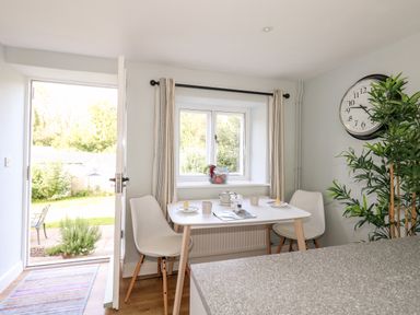 A dining area with a white table and two chairs near a window and an open door at Dairy Cottage in Abbotsbury