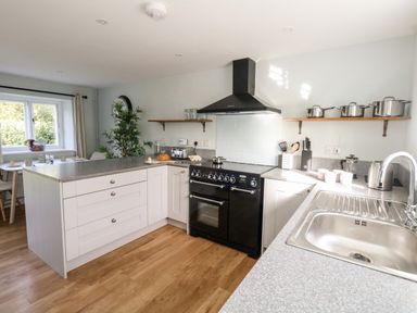 A kitchen with white cabinets a black stove and oven a sink countertop with kitchen utensils and pots on shelves at Dairy Cottage in Abbotsbury