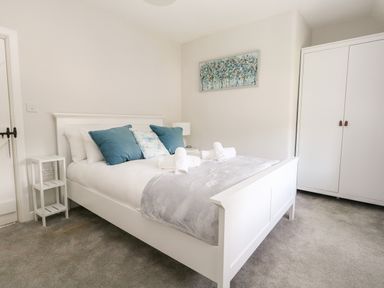 A bedroom with a white bed with blue and white pillows a white bedside table a white wardrobe and a painting on the wall at Dairy Cottage in Abbotsbury