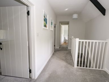 A hallway with carpeted floor white walls and doors white railings and framed pictures at Dairy Cottage in Abbotsbury