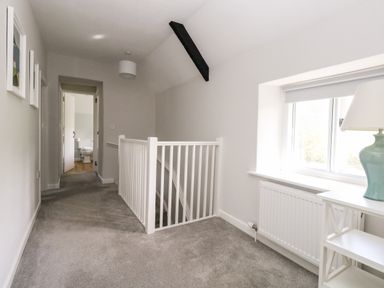 A hallway with carpeting a staircase with white railing and a bathroom at the end at Dairy Cottage in Abbotsbury