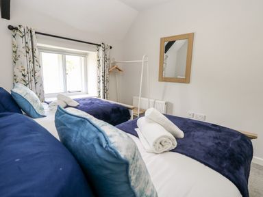 A bedroom with two single beds with blue bedding a window with floral curtains a wall mirror and a clothes rack at Dairy Cottage in Abbotsbury