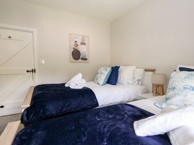 A bedroom with two single beds with white bedding and dark blue throws at Dairy Cottage in Abbotsbury