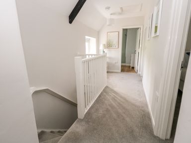 A carpeted upstairs hallway with a white banister a window and a lamp at Dairy Cottage in Abbotsbury