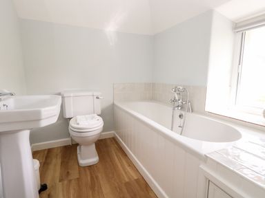 A bathroom with a bathtub a toilet and a pedestal sink with wooden flooring at Dairy Cottage in Abbotsbury