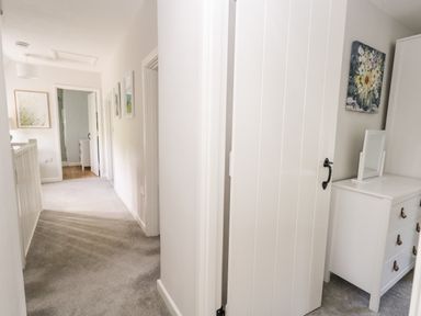 A hallway with carpet and white walls with doors leading to rooms and a white dresser with a mirror in one room at Dairy Cottage in Abbotsbury
