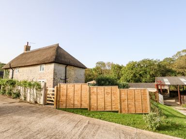 A stone cottage with a thatched roof near wooden fences and greenery at Dairy Cottage in Abbotsbury