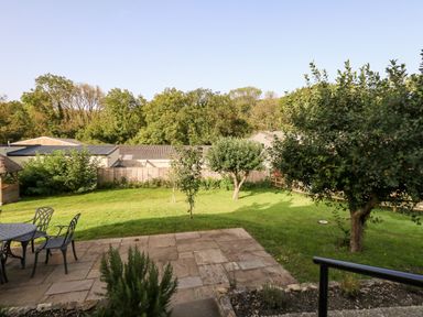 A backyard with a stone patio and metal table with chairs with grass and trees at Dairy Cottage in Abbotsbury