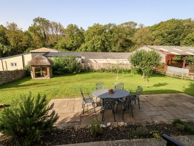 A garden with a patio table and chairs and a thatched gazebo at Dairy Cottage in Abbotsbury