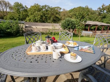 An outdoor table with cups plates a teapot a French press and pastries in a garden at Dairy Cottage in Abbotsbury