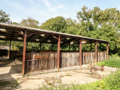 An open sided metal and wood structure in a rural area with trees in the background at Dairy Cottage in Abbotsbury