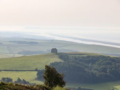 A landscape with a hilltop building overlooking fields and a river in the distance