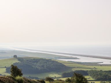 A view of green hills and trees overlooking a river and a coastline at Dairy Cottage in Abbotsbury