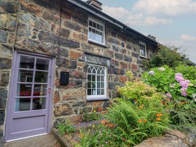 A stone wall with a front door and windows at Riverside Cottage in Beddgelert