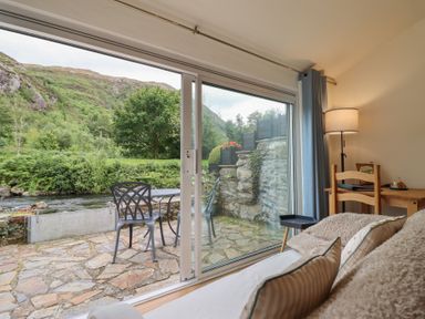 A living room with a view of a river and mountains at Riverside Cottage in Beddgelert