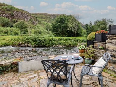 A table and chairs by a river at Riverside Cottage in Beddgelert