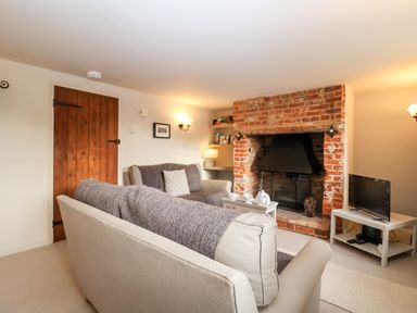 A living room with a brick fireplace two sofas a wooden door and a television at 2 Mosses Cottage in Friston