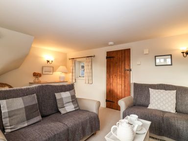 A living room with two sofas a tray with a teapot and cups on a table a wooden door and wall lights at 2 Mosses Cottage in Friston
