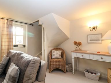 A living room with a sofa a wicker chair a white desk with drawers and a lamp at 2 Mosses Cottage in Friston