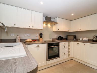 A kitchen with white cabinets wooden countertops an oven microwave kettle and a cutting board with bread and tomatoes at 2 Mosses Cottage in Friston