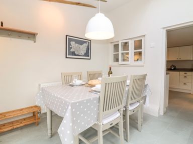 A dining area with a polka dot tablecloth on a table set for four with chairs and a pendant light at 2 Mosses Cottage in Friston