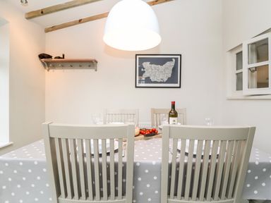 A dining room with a table covered by a polka dot tablecloth and four chairs at 2 Mosses Cottage in Friston