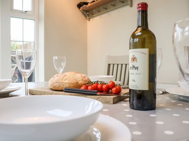 A dining table with a bottle of wine bread tomatoes cutting board and wine glasses at 2 Mosses Cottage Friston